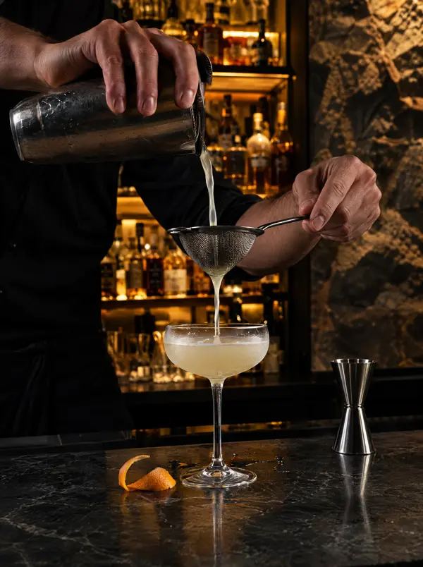Barkeeper giesst einen Cocktail in ein Coupe-Glas